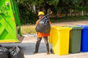 Lenny began stumbling through the junk to the other side of the nearby landfill after picking up the mound of trash with his greasy, blackened gloves